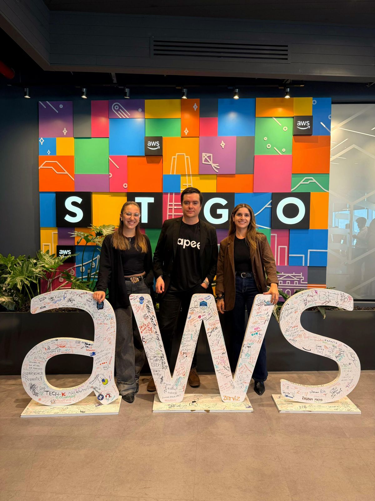 Equipo Hapee en oficinas AWS Santiago con muro AWS y letras STGO firmadas
